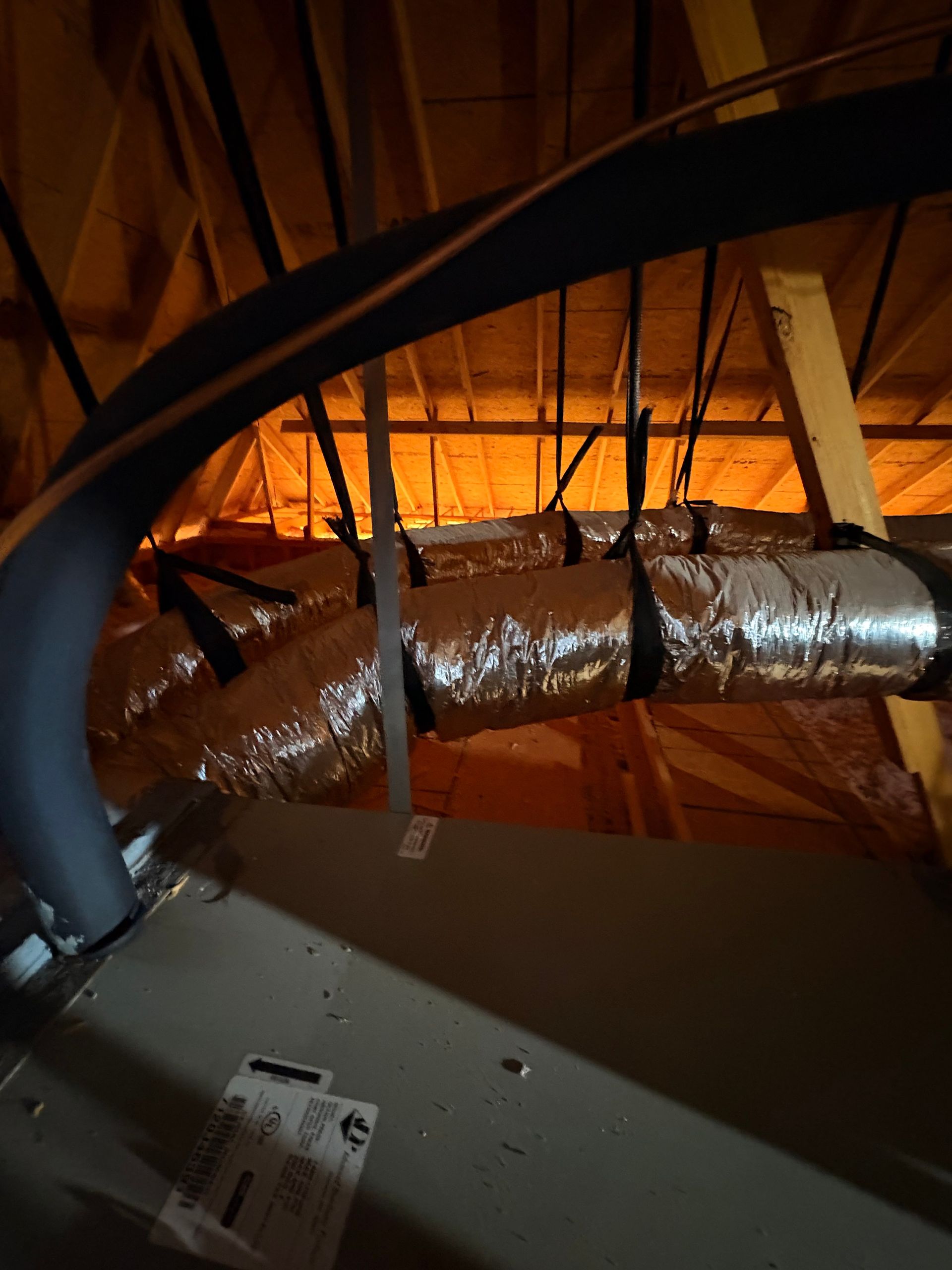 Silver insulated HVAC duct in an attic with wooden rafters and orange lighting