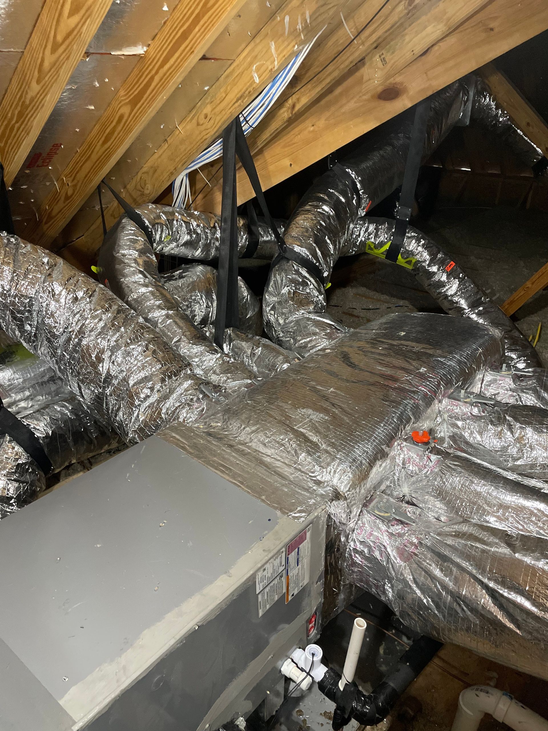 Attic crawlspace with insulated HVAC ducts, exposed wooden rafters, and a gray equipment unit.