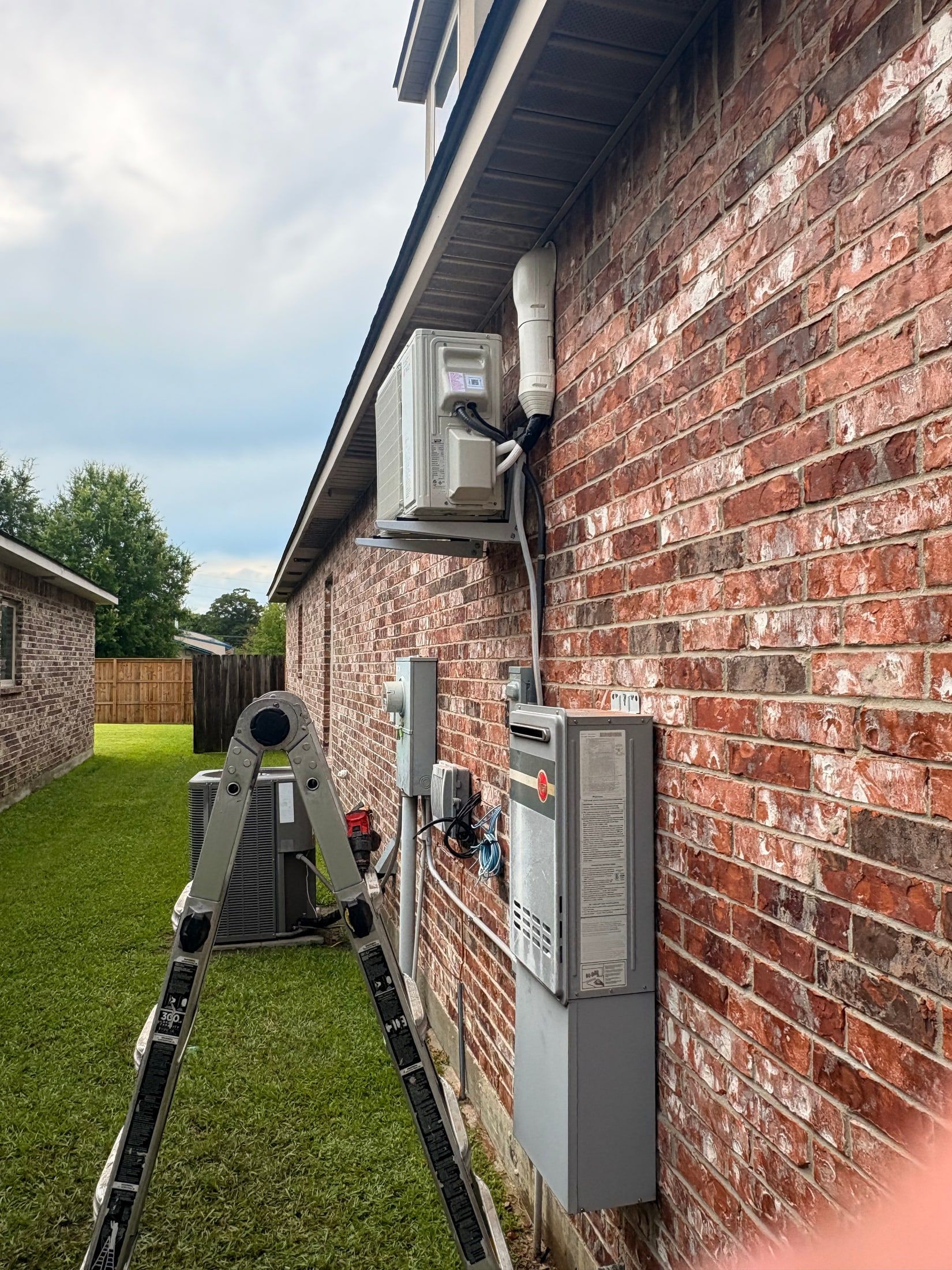 Side view of a brick house with utility boxes and conduit along the exterior wall
