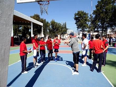 Entrenador de baloncesto dando instrucciones a un equipo de jugadores que visten camisetas rojas en una cancha azul.