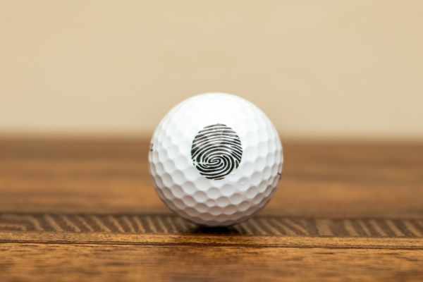 A golf ball with a fingerprint on it is sitting on a wooden table.