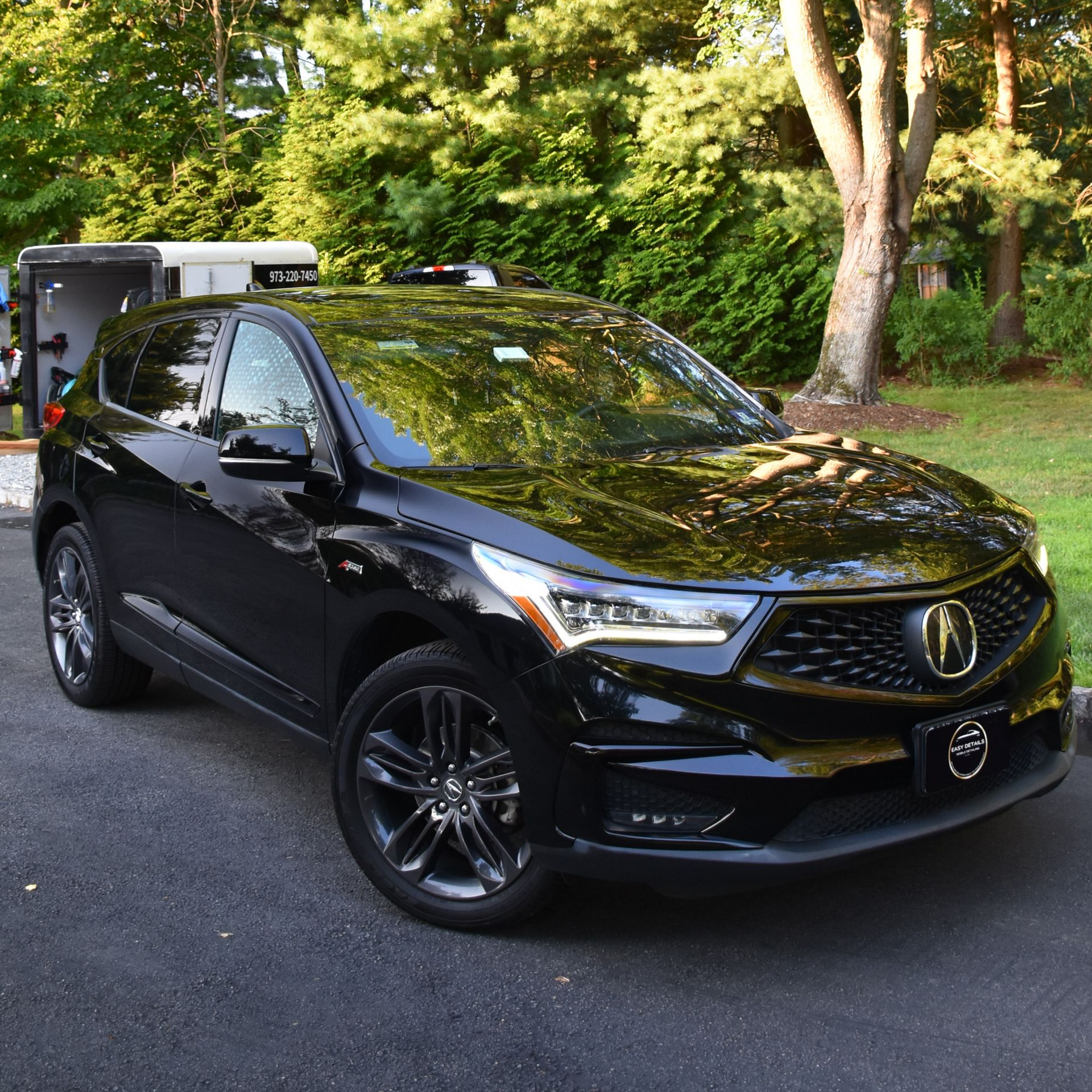 Black Acura RDX SUV parked on asphalt driveway, with trees in the background.
