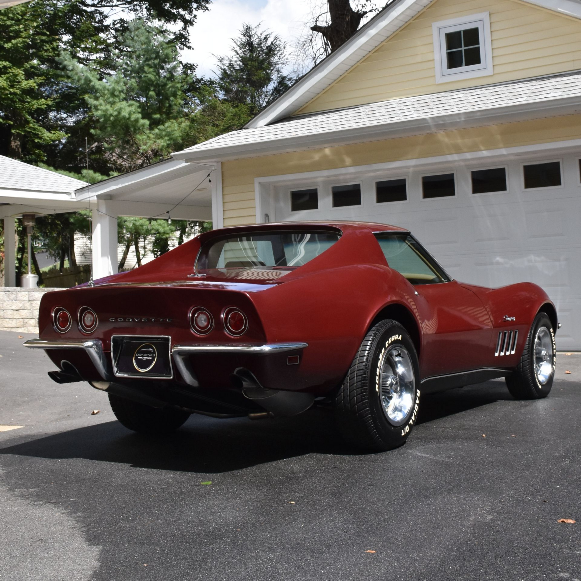 Red 1969 Chevrolet Corvette coupe parked in front of a yellow house with a garage.