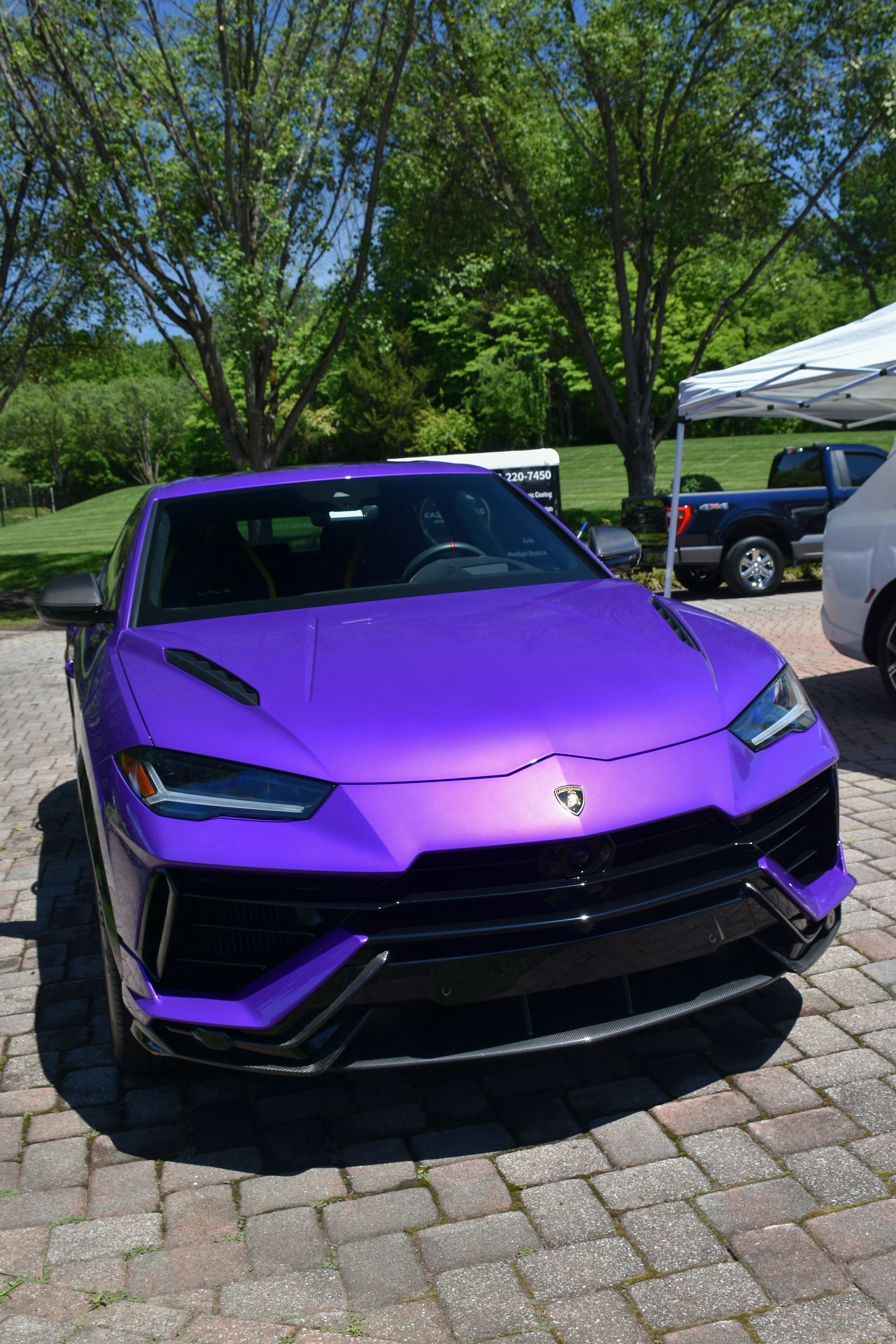 Purple Lamborghini SUV parked on a cobblestone driveway under trees