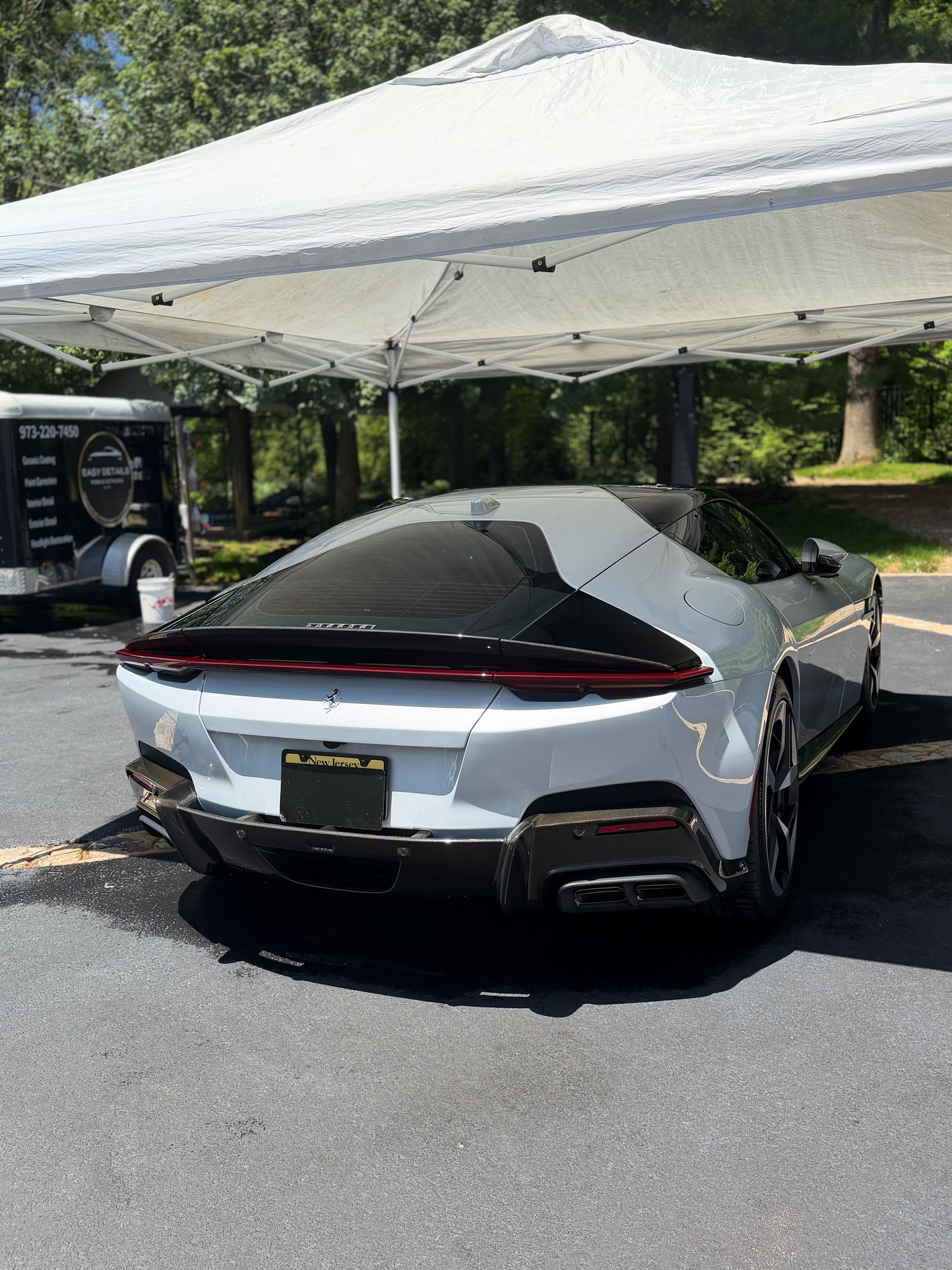 Silver sports car parked under a white canopy at an outdoor event, rear view.