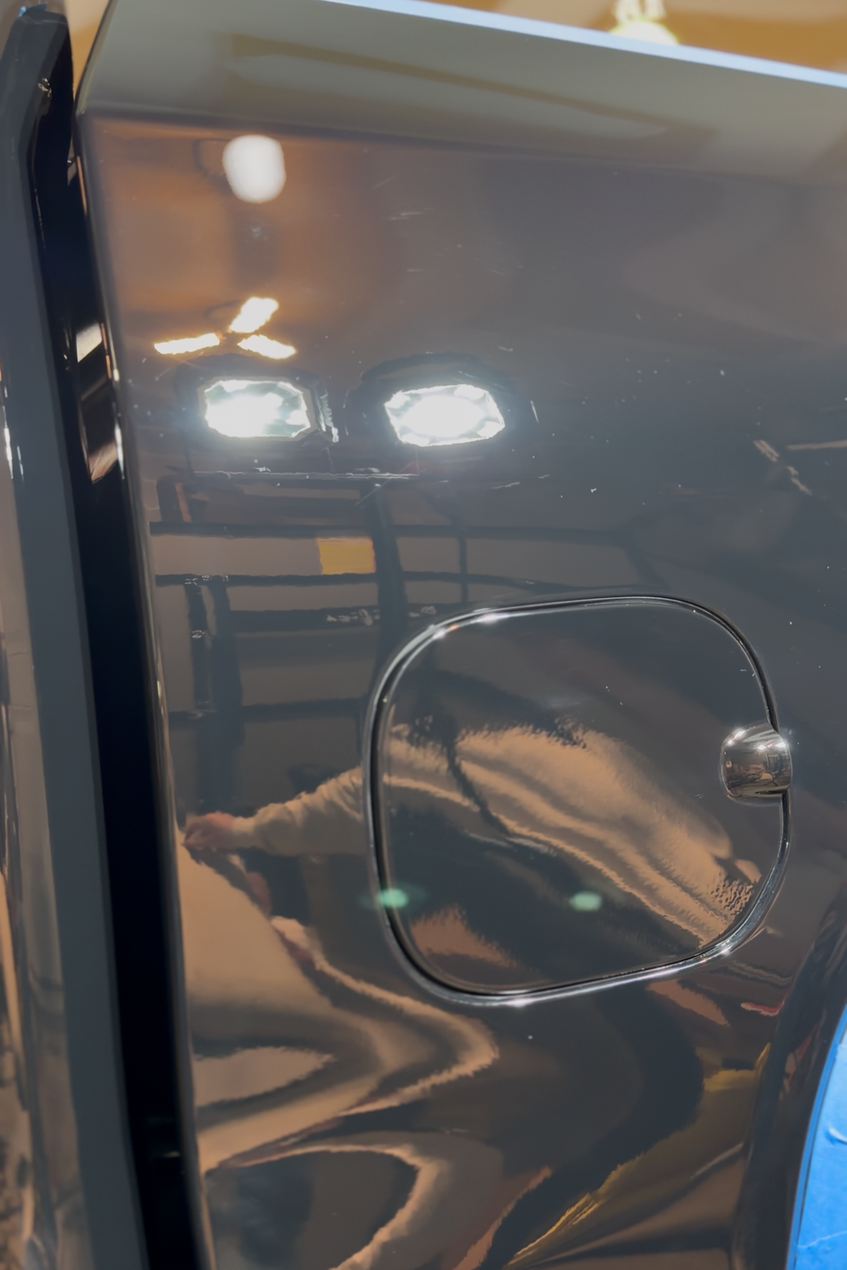 Close-up of a dark car body panel with a square fuel door and glossy reflections