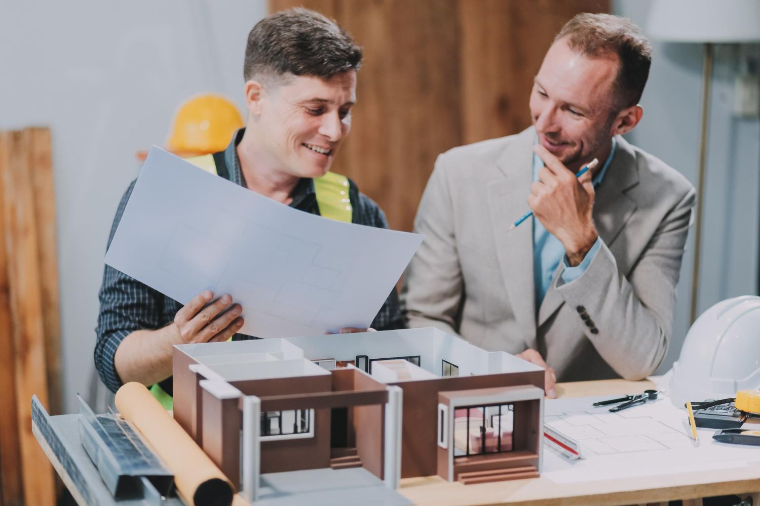 Two colleagues review architectural plans beside a building model at a desk