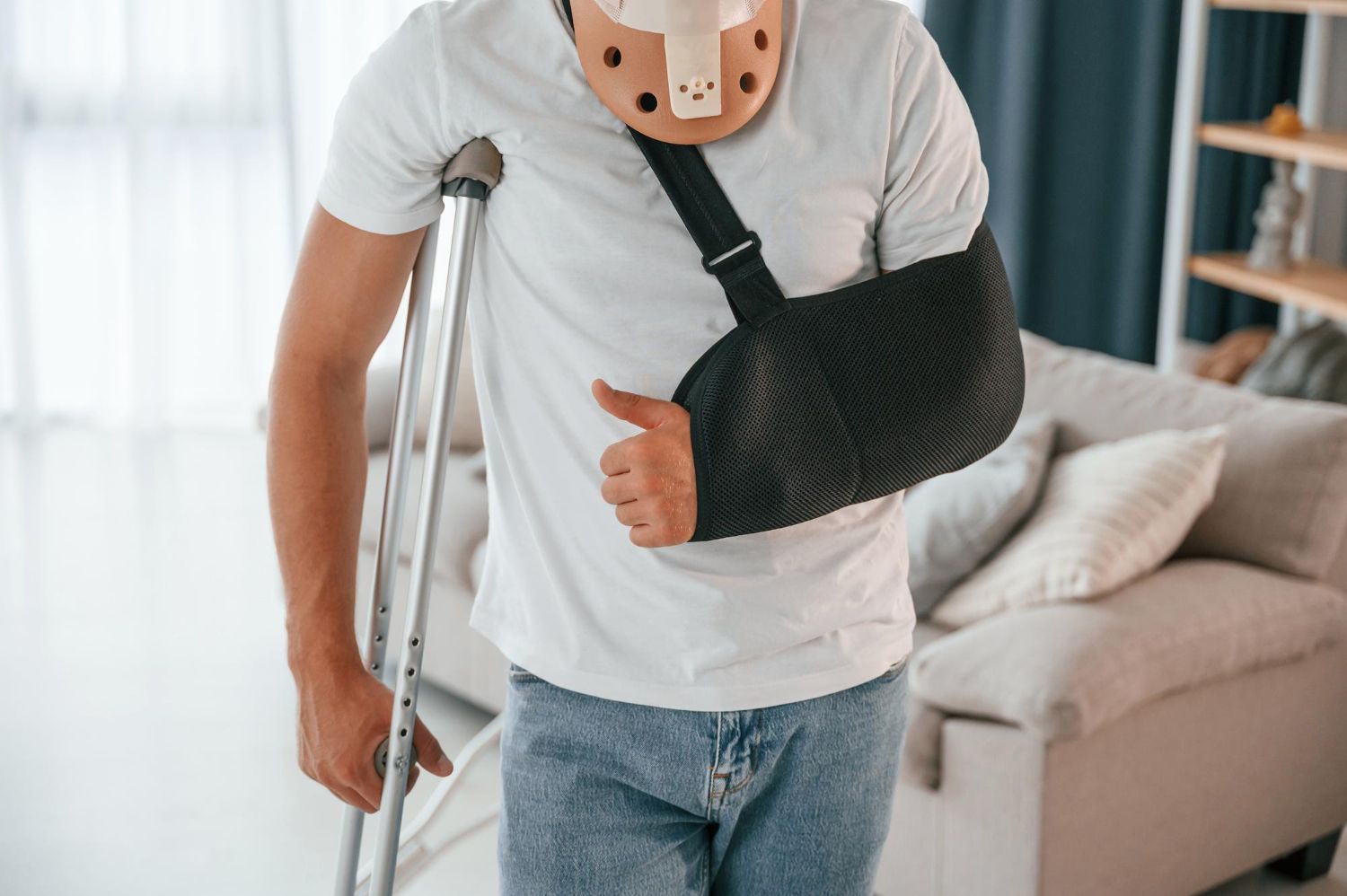 Person with arm sling and crutches standing in a living room