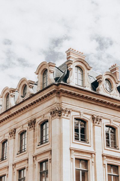 Ornate beige corner building with balconies and dormer windows against a cloudy sky
