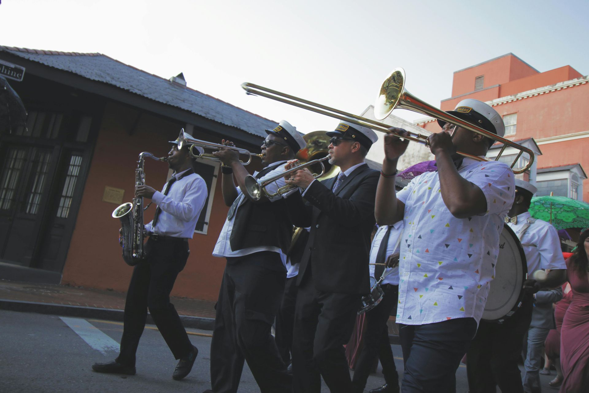 Brass band marching outdoors, playing trombones and trumpets in front of buildings