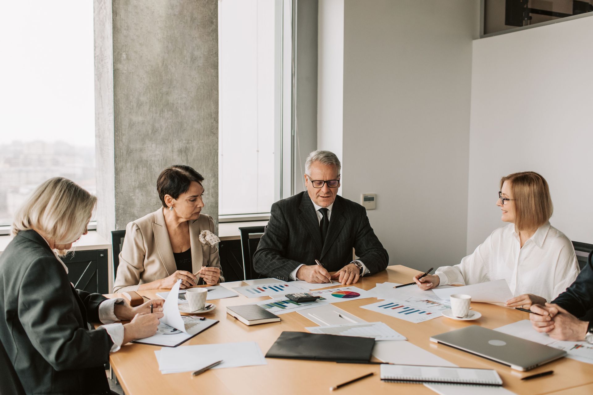 People in a meeting around a conference table reviewing papers and laptops in a bright office