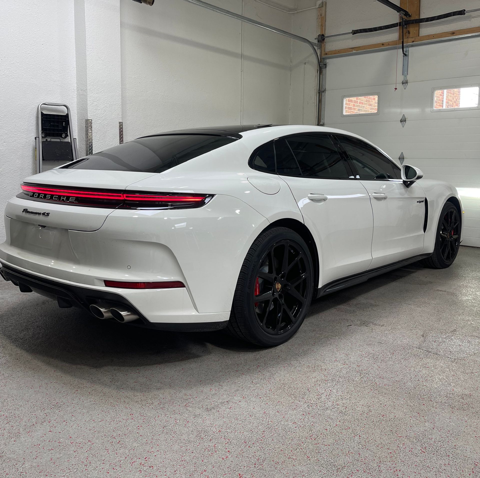 White Porsche Panamera parked inside a garage; black wheels, tinted windows, and a red taillight.