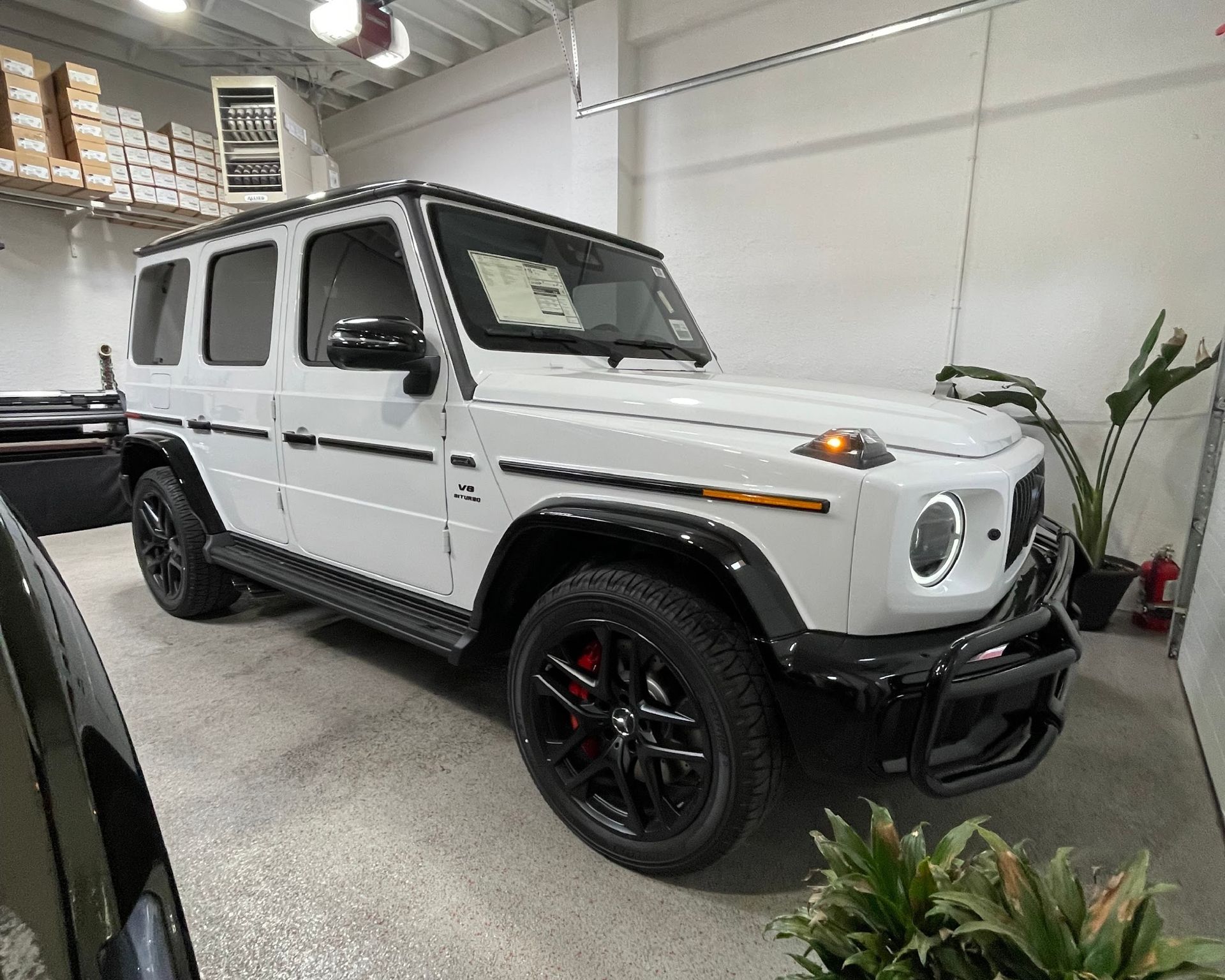 White Mercedes-Benz G-Wagon SUV with black accents, red brake calipers, parked inside a showroom.