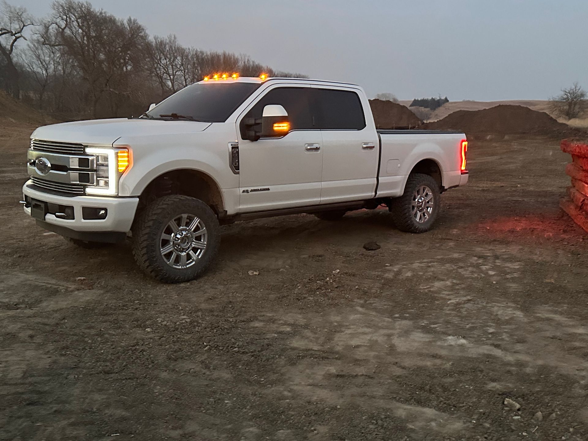 White Ford pickup truck on dirt. Evening setting, lights on.