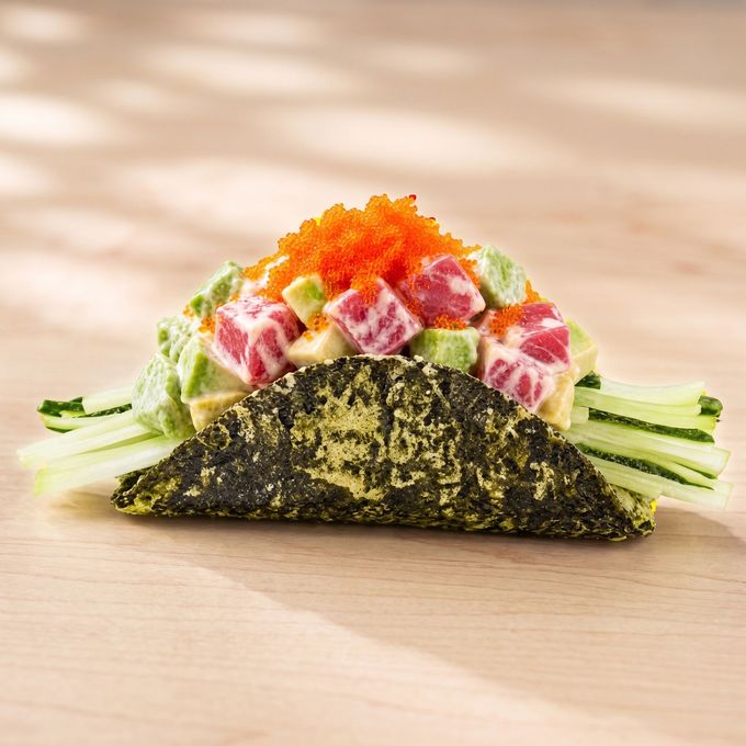 Nori taco shell filled with diced fish, avocado, cucumber, and orange roe on a wooden surface