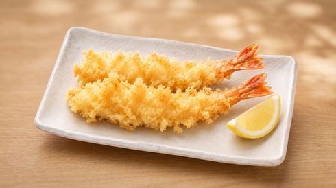 Two shrimp tempura on a white plate with a lemon wedge, served on a wooden table