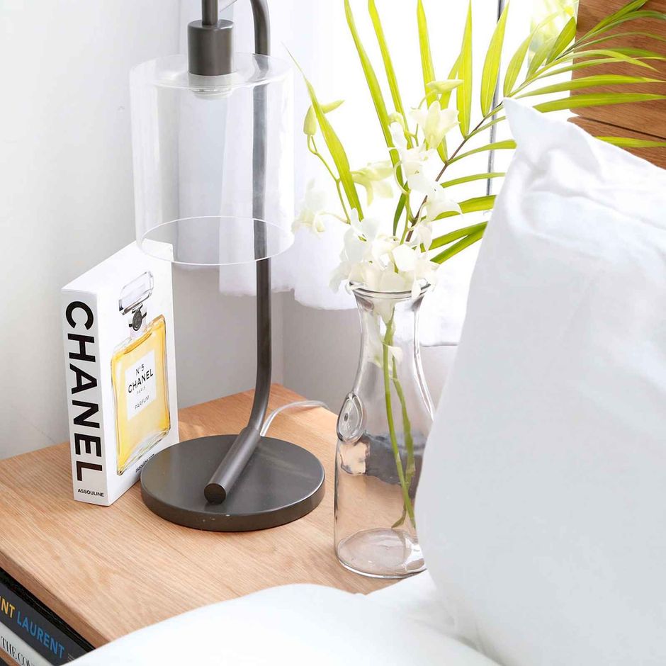 Nightstand with a lamp, a vase of flowers, and a Chanel book.
