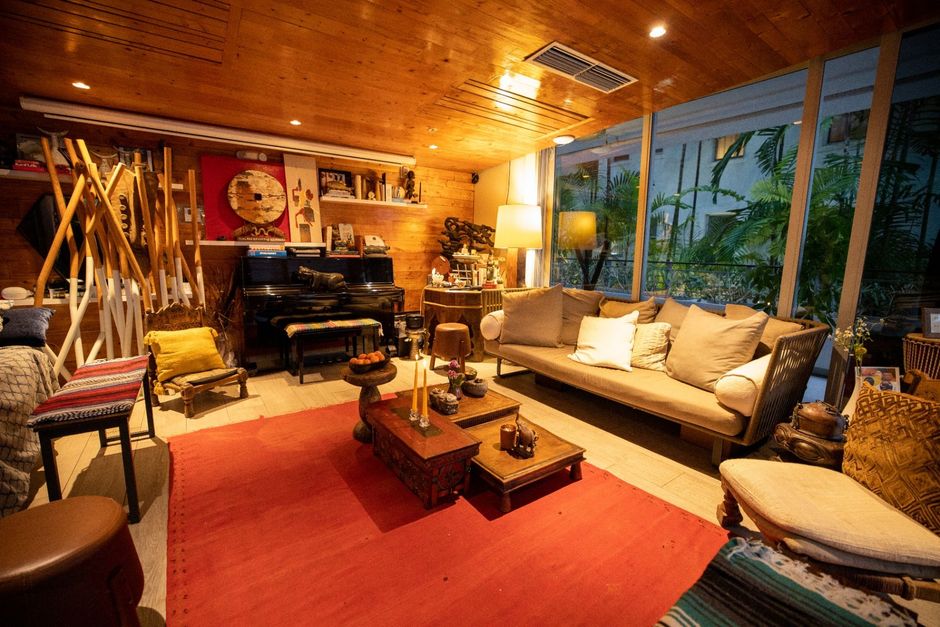 Cozy living room with red rug, beige sofa, piano, wooden decor, and large windows looking onto greenery