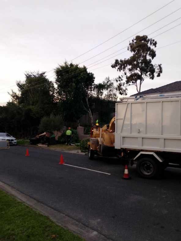 Roadwork crew beside a white truck on a street at dusk, with orange cones and equipment.