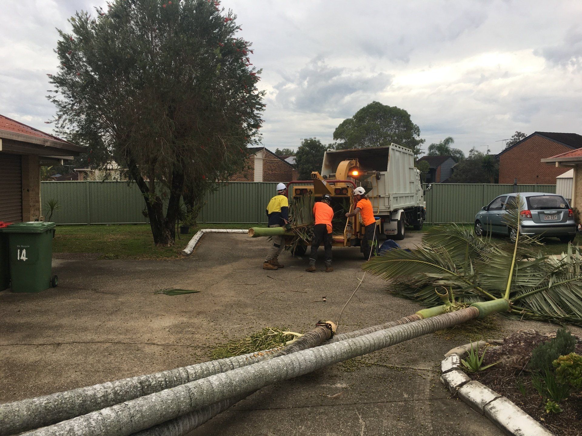 Workers in orange vests clear storm debris beside a truck on a suburban street