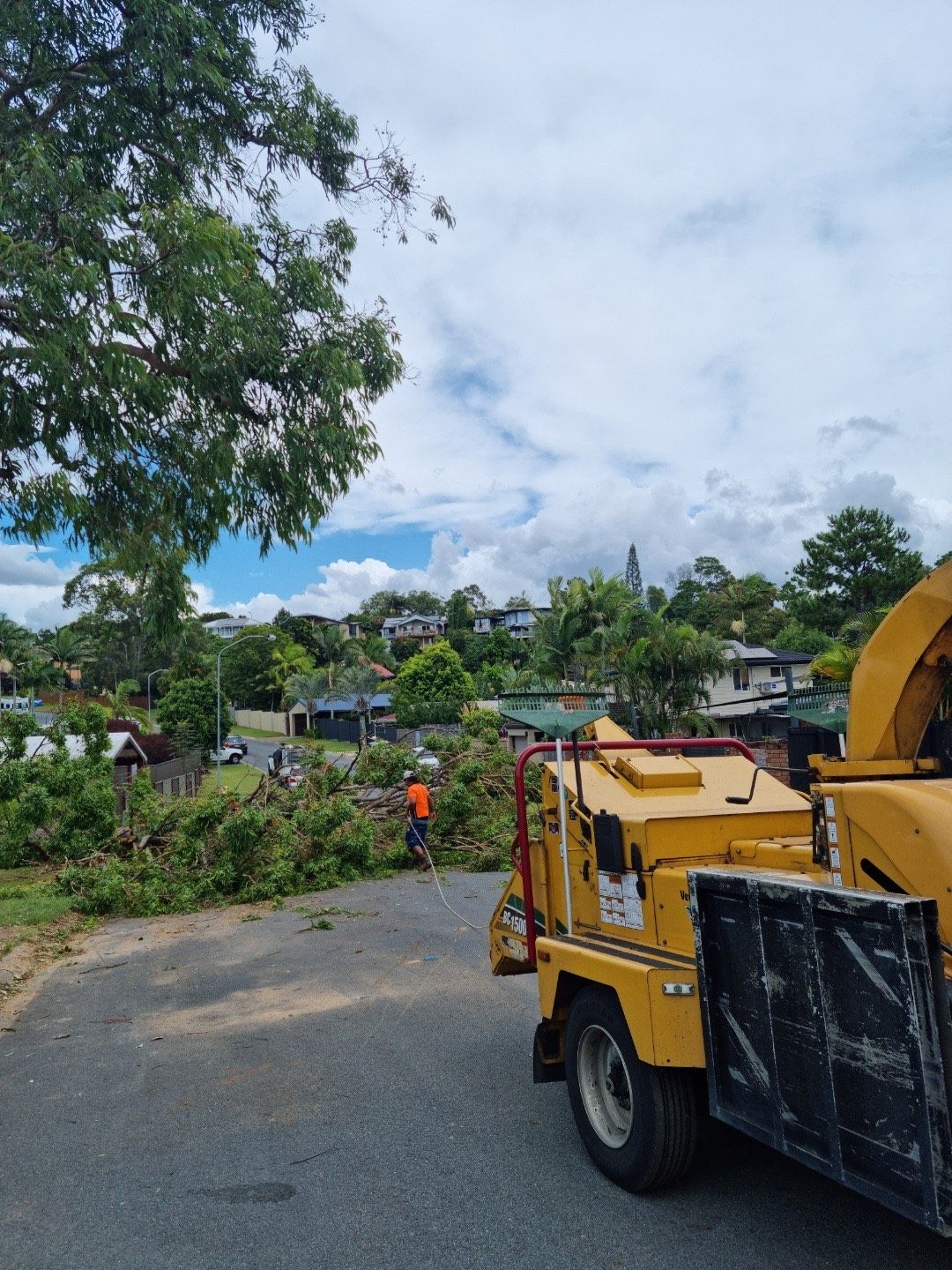 Yellow utility truck on a rural road with workers and trees under a cloudy sky
