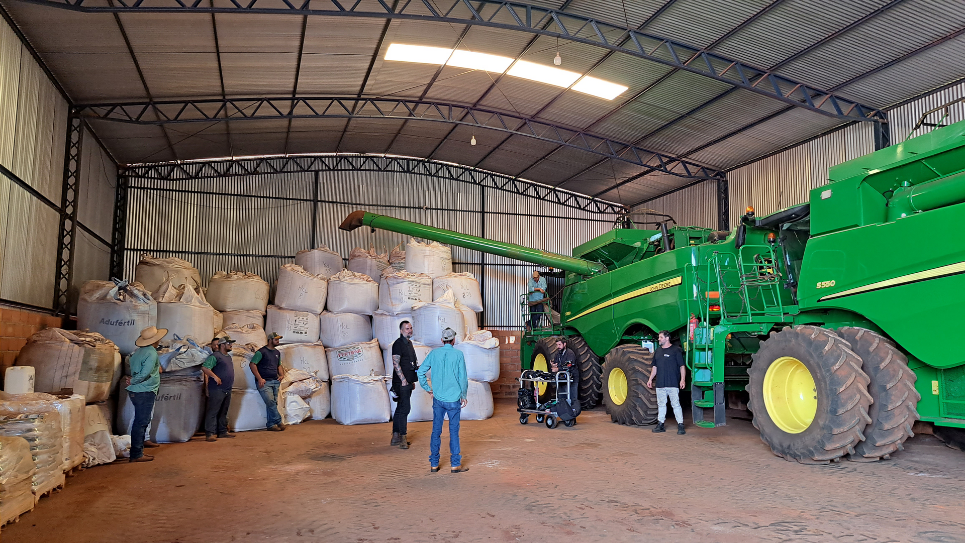 A group of people are standing in a warehouse next to a john deere combine harvester.