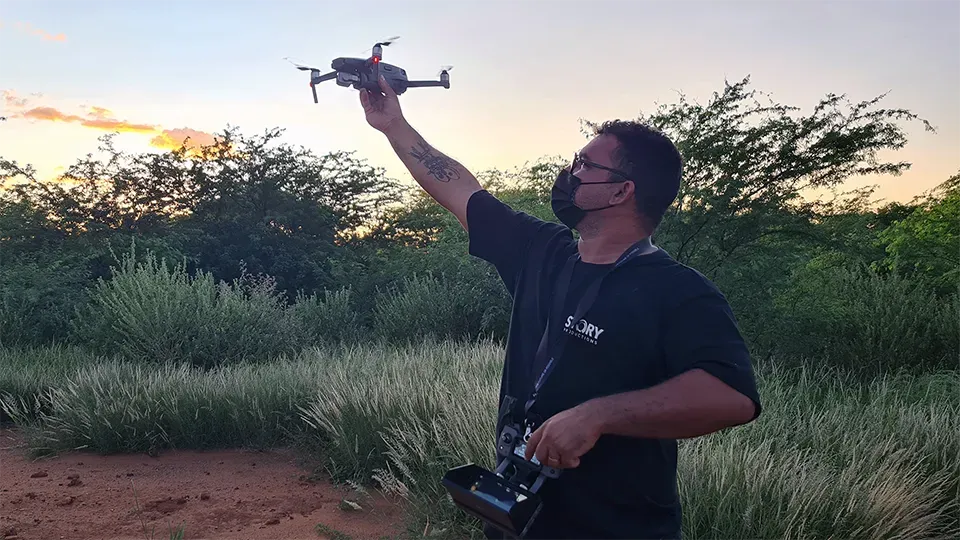 A man is holding a drone in his hand in a field.