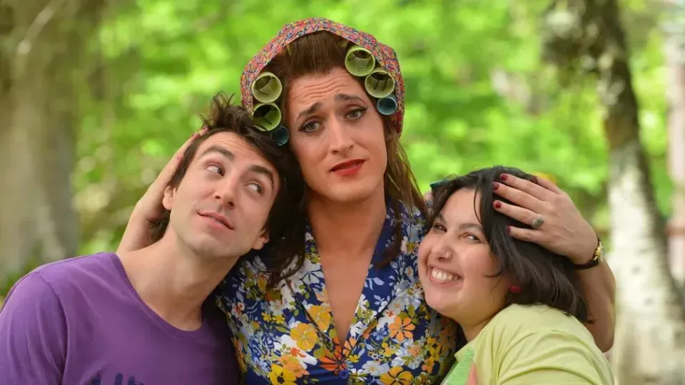 A man and two women are standing next to each other . the woman is wearing curlers on her head.