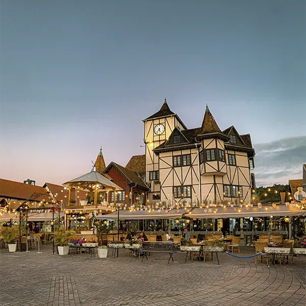 A large building with a clock tower is surrounded by tables and chairs.