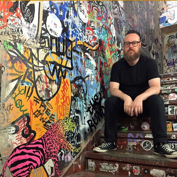 Regisseur und Drehbuchautor Dennison Ramalho sitzt auf den Stufen einer Treppe A man is sitting on a set of stairs in front of a wall with graffiti on it