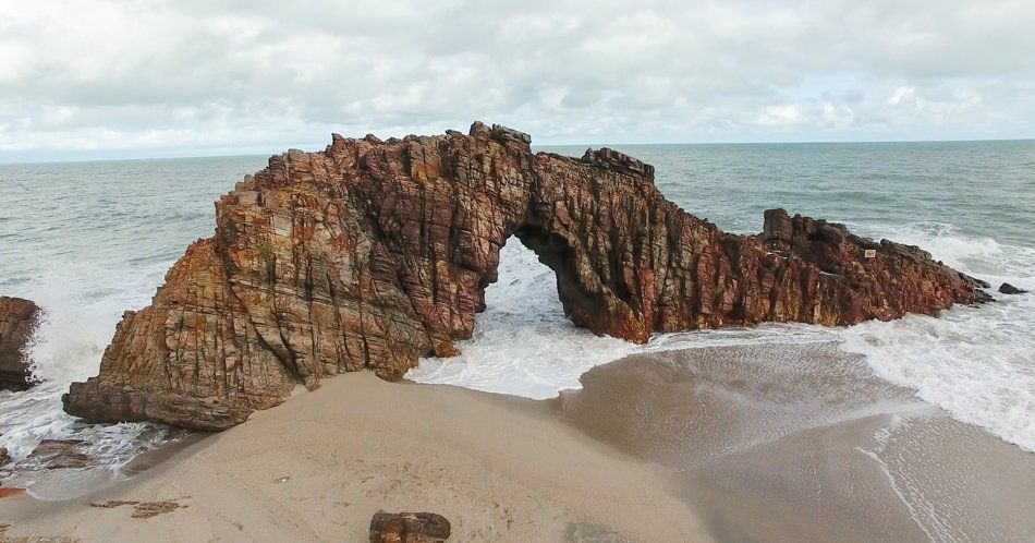 A large rock formation on a beach next to the ocean.