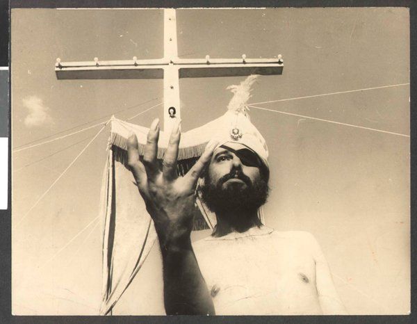 José Mojica Marins alias Coffin Joe, in einer Szene aus dem Film „O profeta“ A man is holding a cross over his head in a black and white photo.