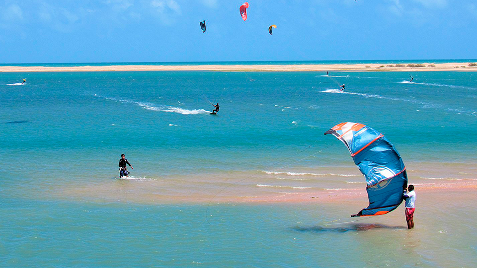 Una playa con atletas de Kitesurt A group of people are flying kites in the ocean.