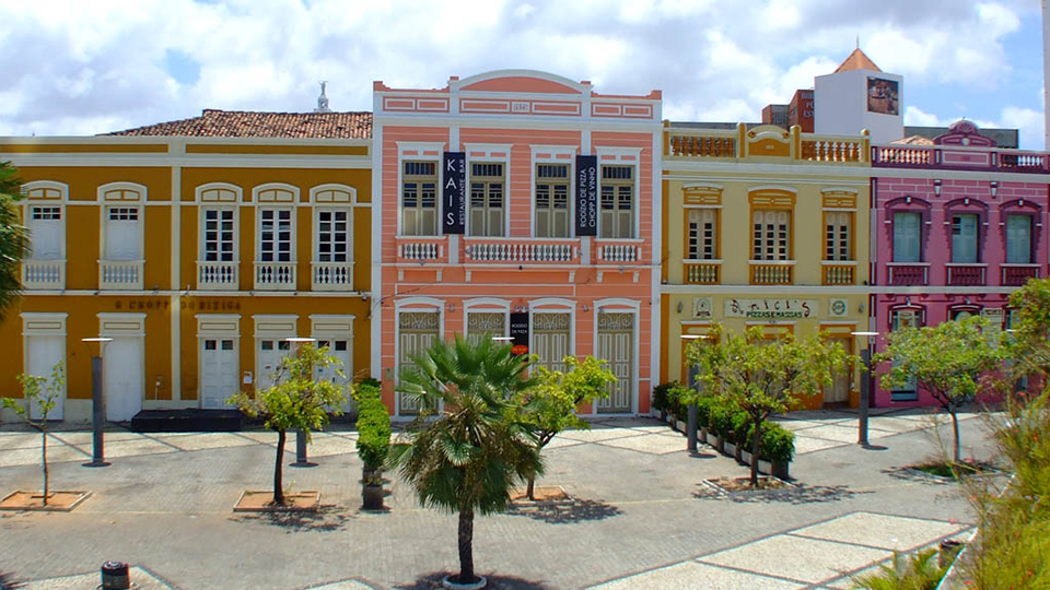 Una cuadra compuesta por edificios colocridos en Ceará A row of colorful buildings with palm trees in front of them