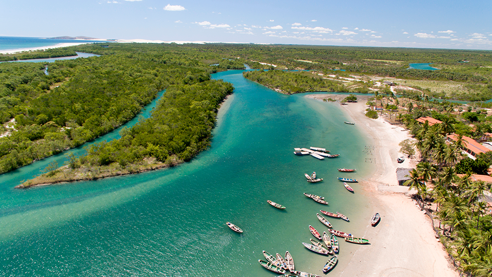 Una vista aerea de una playa con barcos atracados An aerial view of a beach with boats in the water and a river.