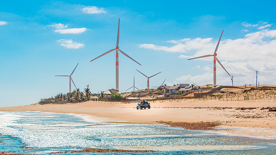 Generadores de energía eolica A car is driving on a beach with wind turbines in the background.