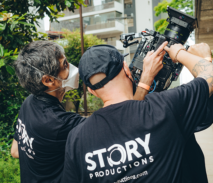 Two men wearing masks are working on a camera.