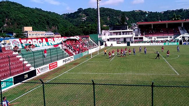 A group of people are playing soccer on a field with a stadium in the background.