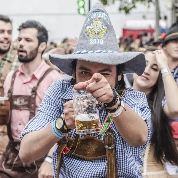 A man wearing a cowboy hat is pointing at the camera while holding a glass of beer