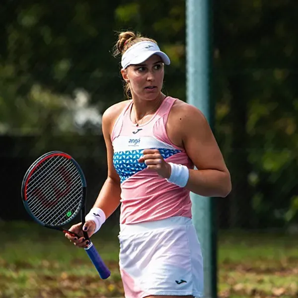 A woman in a pink tank top and white skirt is holding a tennis racquet