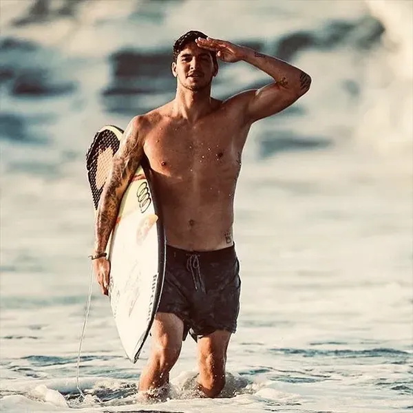A shirtless man is holding a surfboard in the ocean