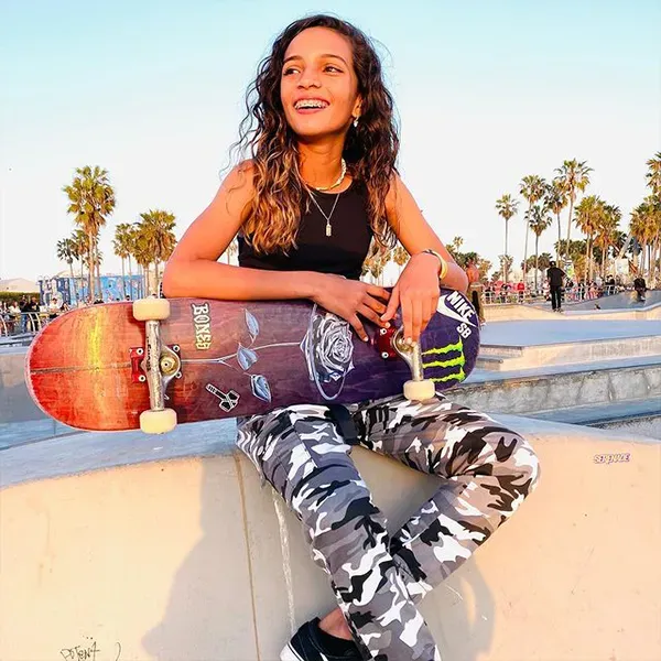 A woman is sitting on a wall holding a skateboard with a monster logo on it