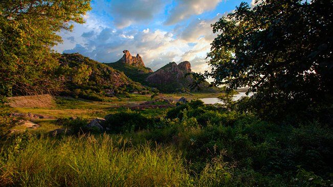 Un paisaje de Quixadá There is a lake in the middle of a field with mountains in the background.
