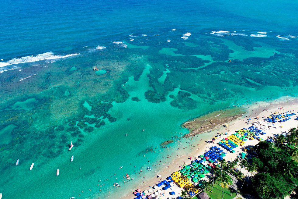Une vue aérienne d'une plage, avec des parapluies et des tentes sur elle et la mer et les récifs
