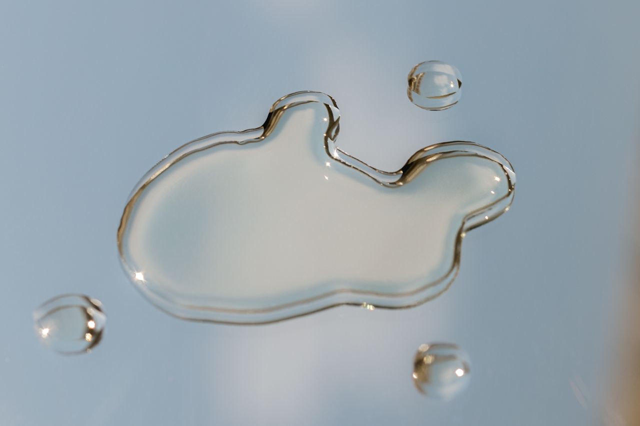 Clear water droplets on a pale blue surface, with one large irregular drop and three smaller drops nearby