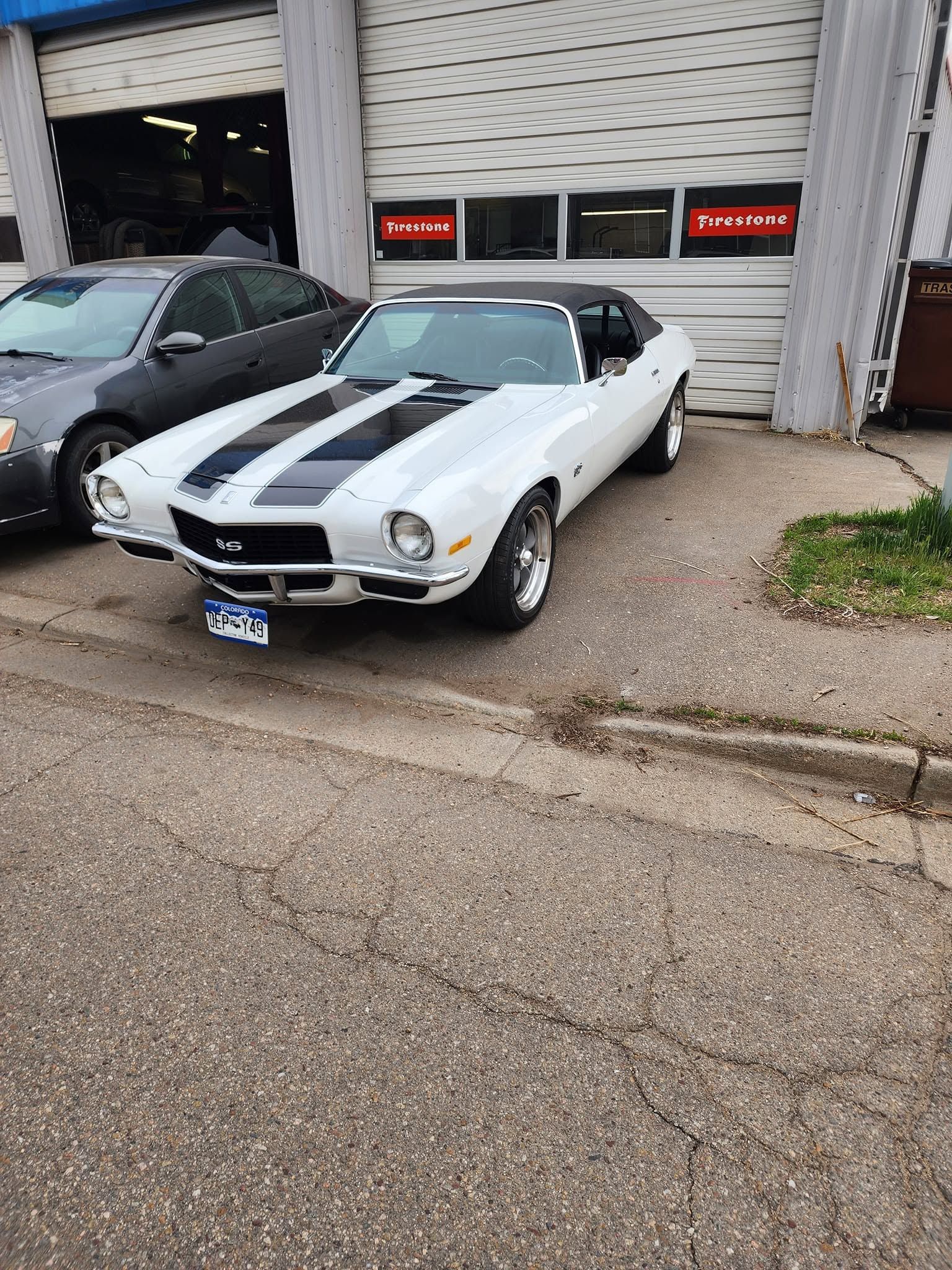 White classic muscle car with black racing stripes parked outside an auto garage.