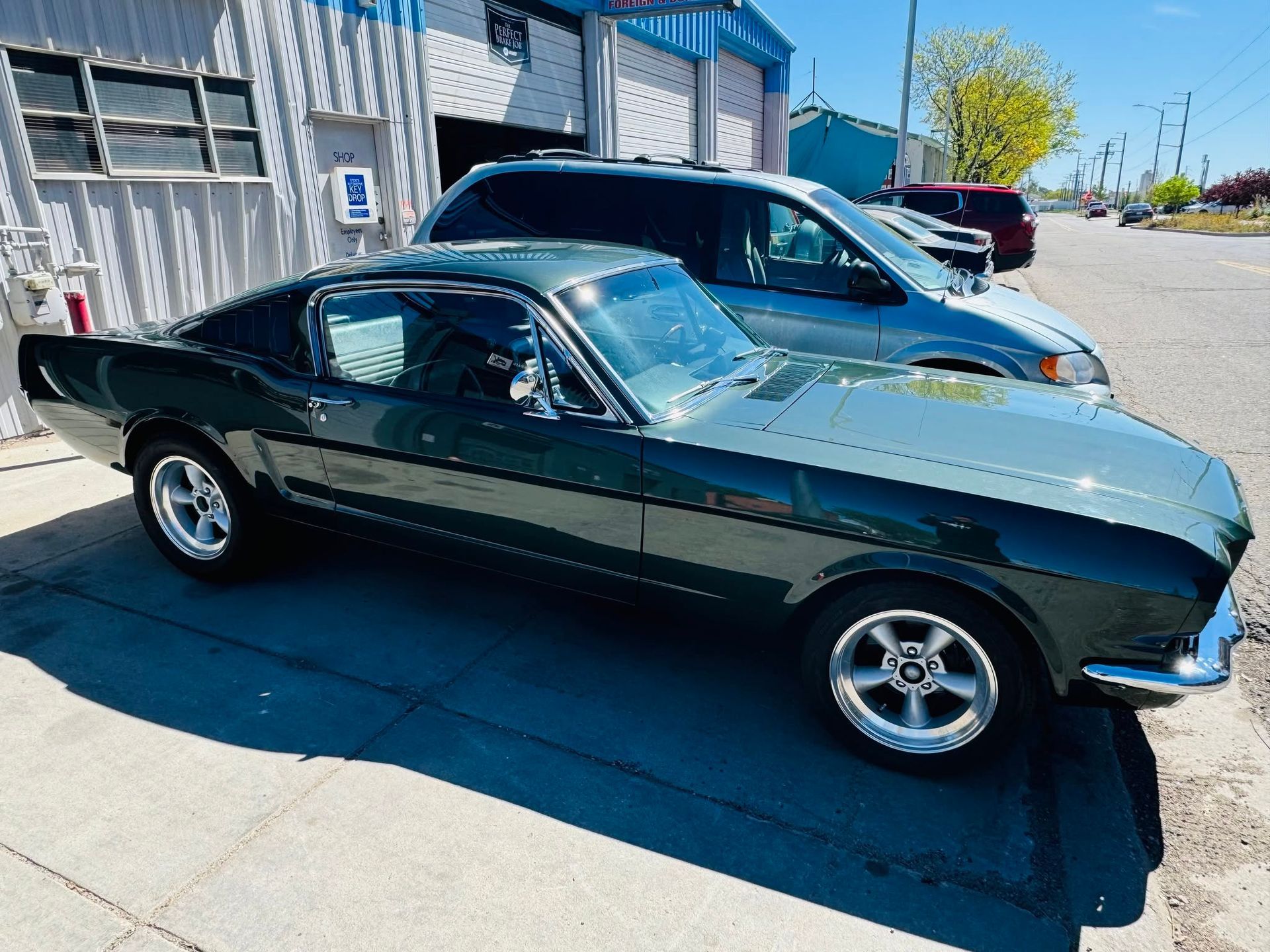 Dark green classic muscle car parked on a sunny street beside a building.