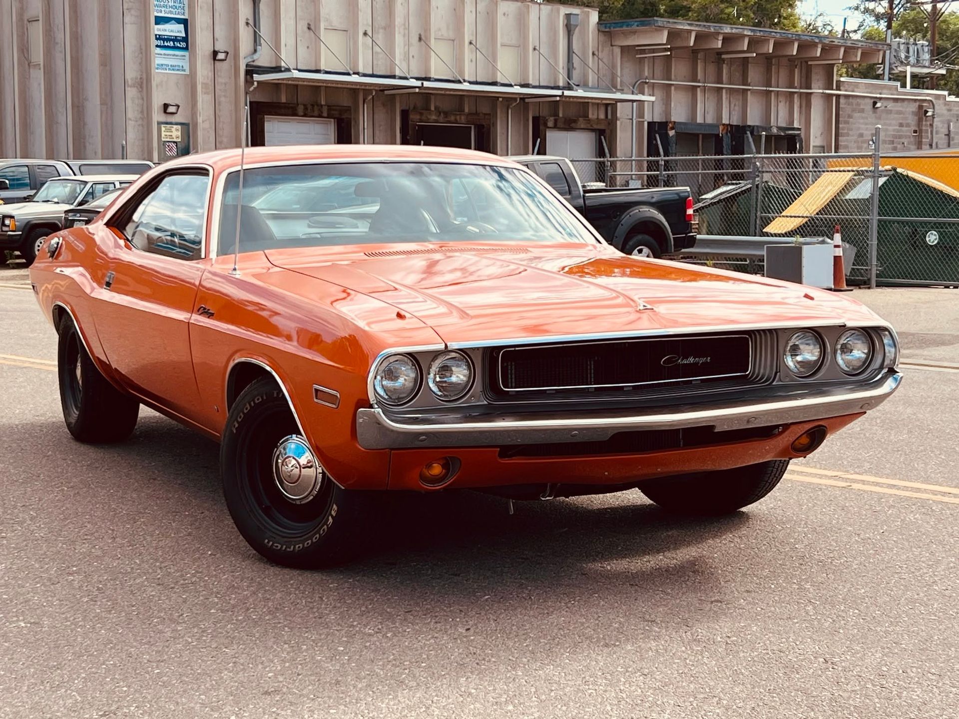 Orange classic muscle car parked on a street, front view with a wooden fence and construction materials behind it