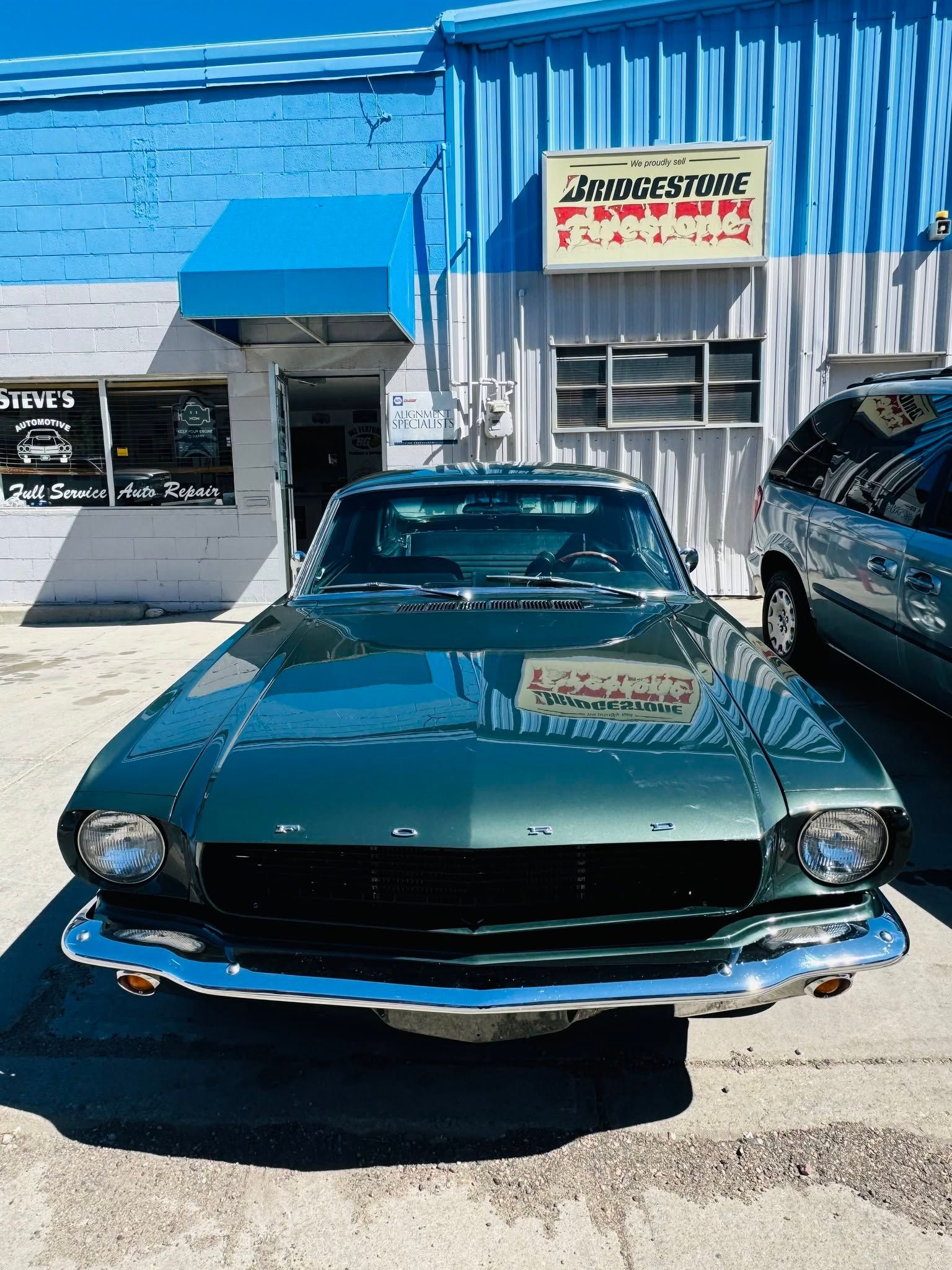 Green classic car parked in front of a blue and white auto repair shop