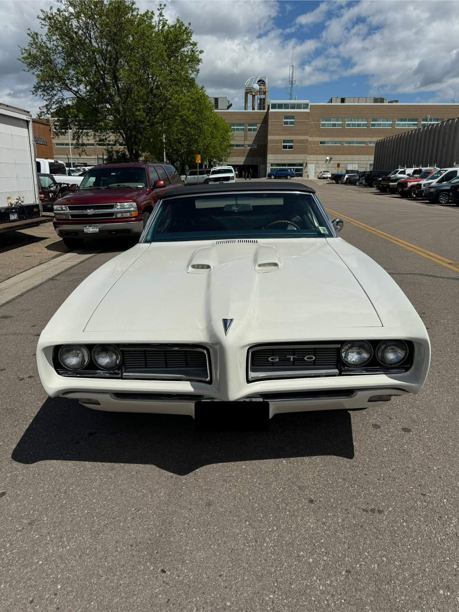 Front view of a white classic muscle car parked in a lot on a sunny day